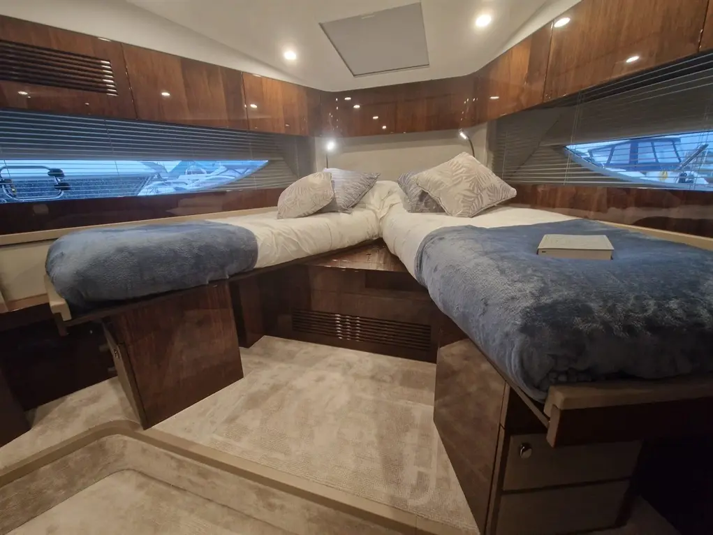 Luxurious boat interior featuring two beds with blue blankets, decorative pillows, and a window overlooking the marina.